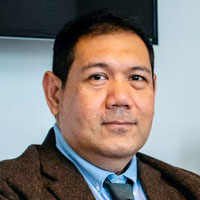 A professional man in a suit and tie sitting in front of a TV.